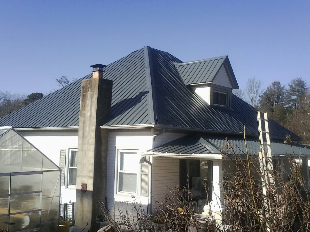 Dark blue standing seam metal roof on a white farmhouse with dormer — Slate & Tile Roof Repair by Roofing Brothers in Galivants Ferry