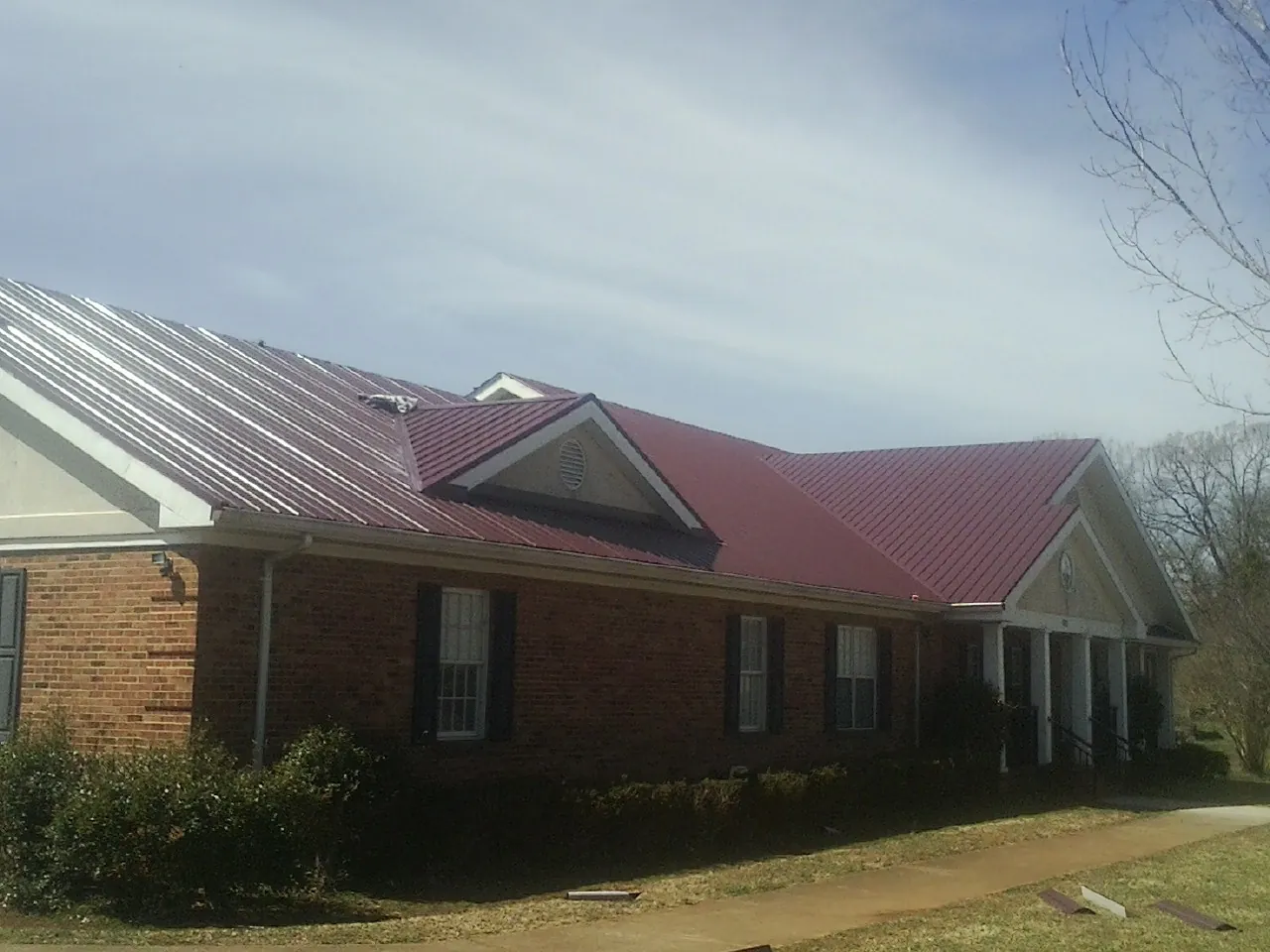 Red metal roof with gabled entries on a long brick building, from a Hail Damage Roof Repair job in Galivants Ferry