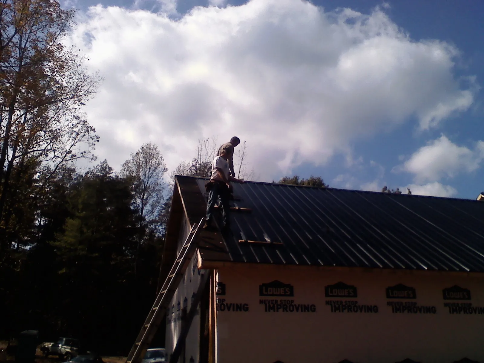 Roofer fastening dark metal panels high against a cloudy sky, from a Roof Inspection job in Galivants Ferry