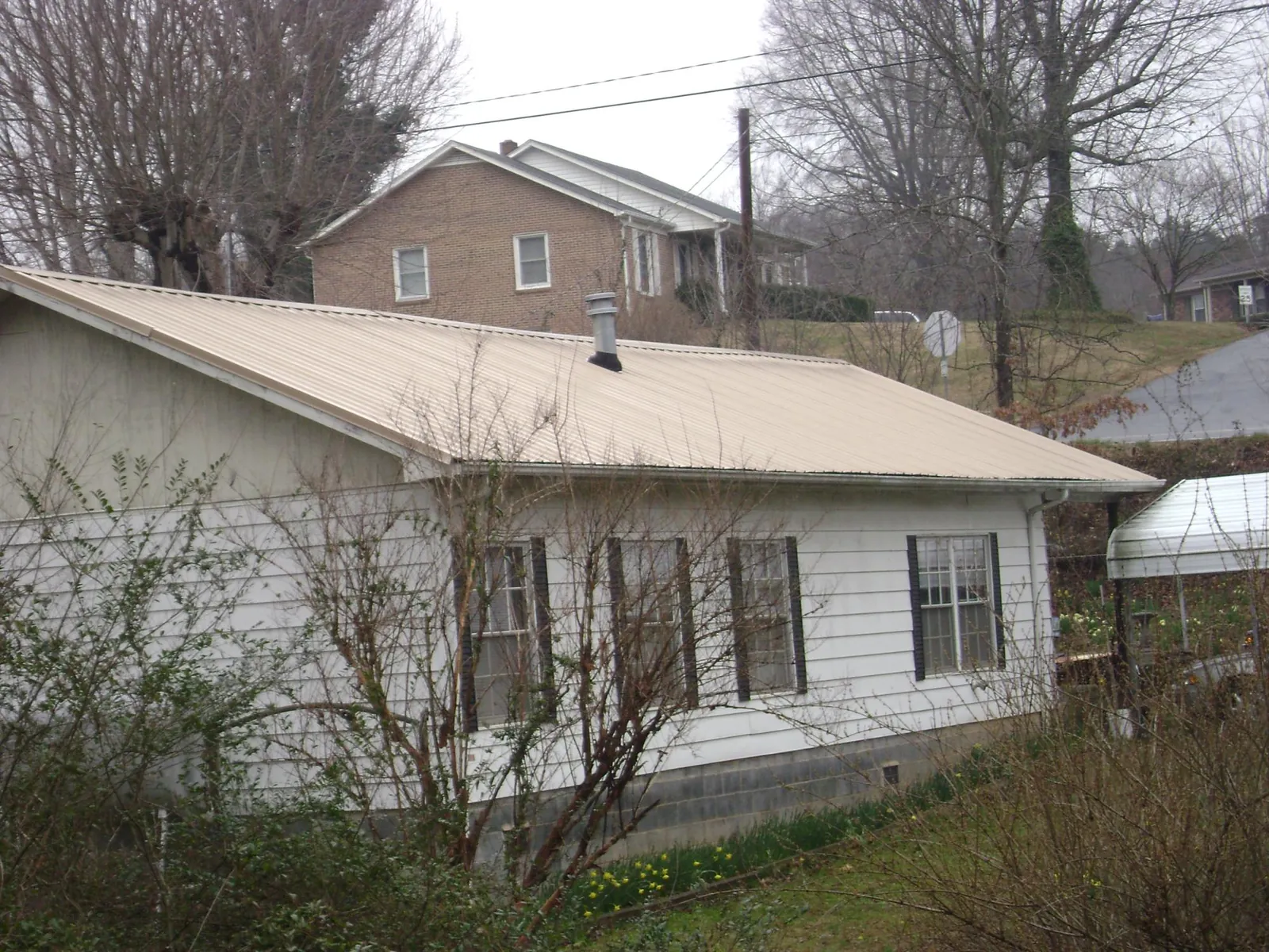 Tan metal roof on a white sided house set into a hillside — Commercial Roofing by Roofing Brothers in Galivants Ferry